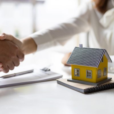 Handshake after reaching a real estate deal. Signing a house rental, mortgage, lease agreement. Real estate agent shakes hands with a client and asks them to legally sign a contract of agreement.